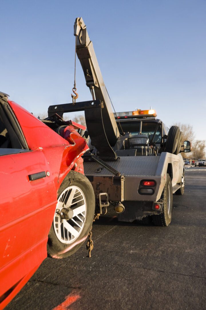 Tow truck transporting damaged red car.